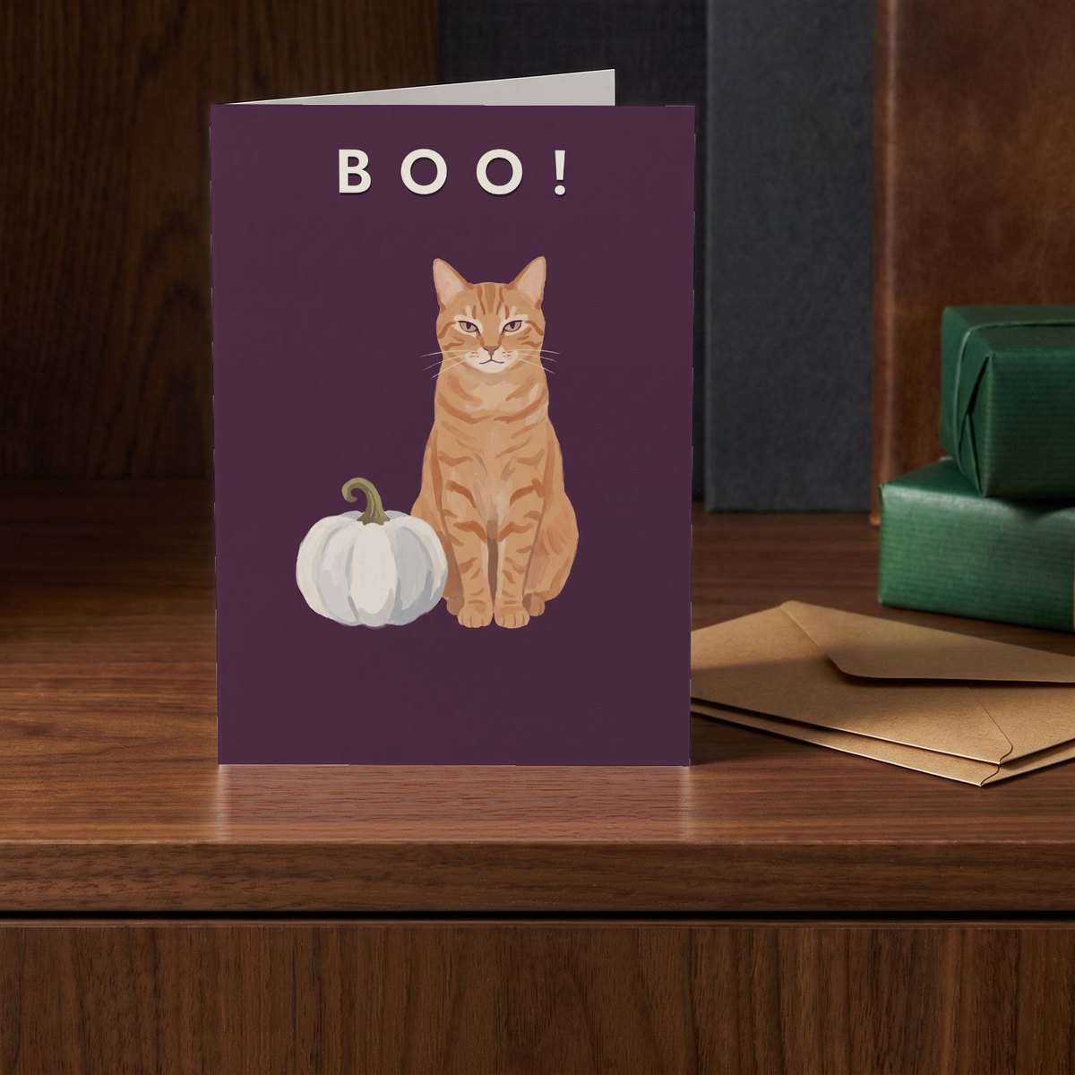 A folded card standing on a walnut sideboard beside two presents wrapped in green