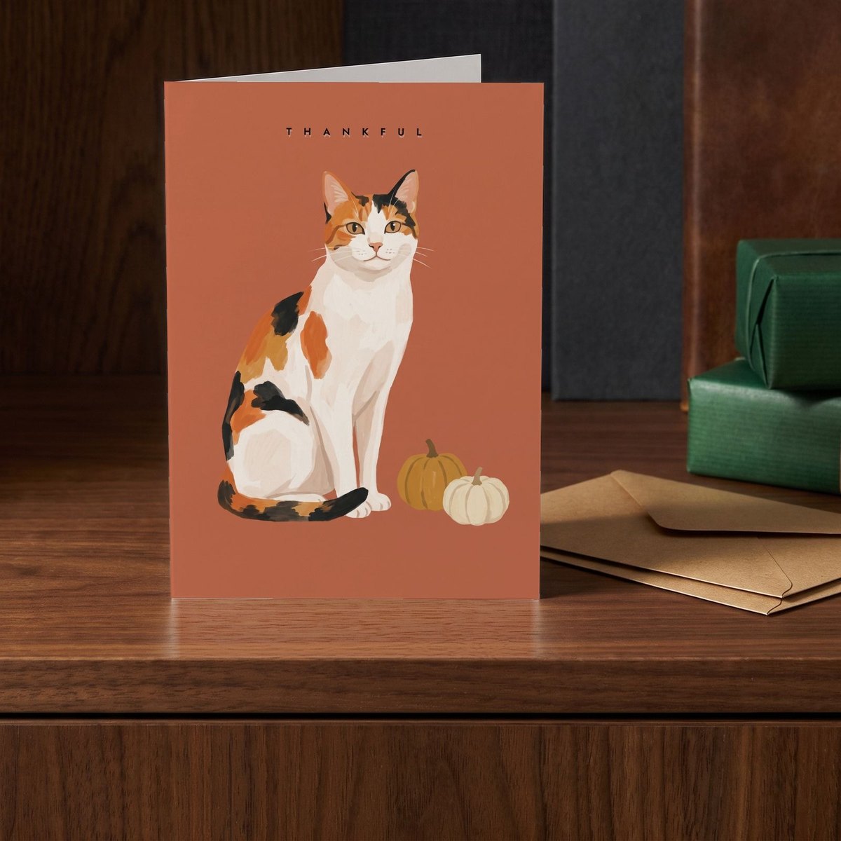 A folded card standing on a walnut sideboard beside two presents wrapped in green