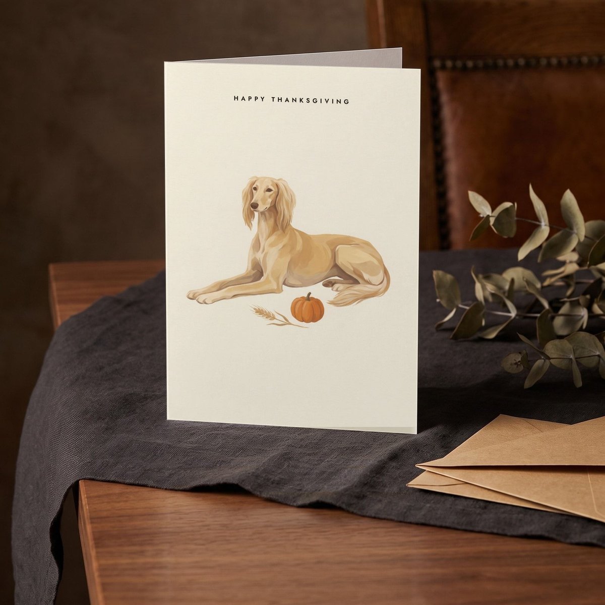A folded card standing on a charcoal linen cloth with a sprig of dried eucalyptus